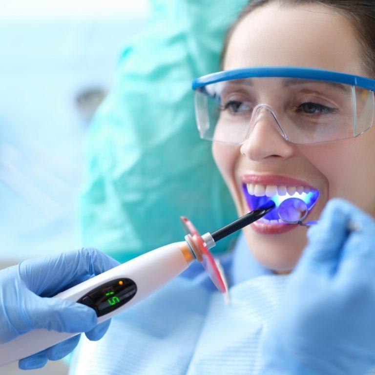 Patient in safety glasses as a curing light is used on her teeth