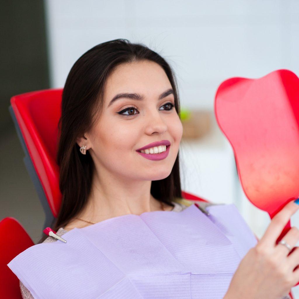 Smiling patient holding a hand mirror in the dental chair