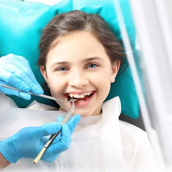 Young child in dental chair smiling while dentist examines teeth with instruments