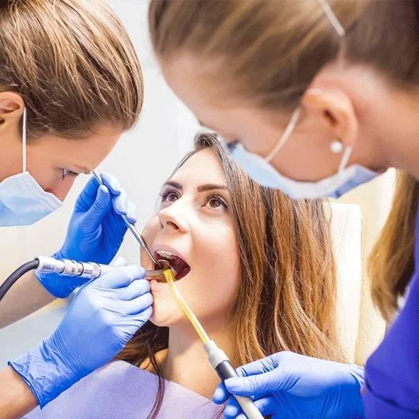 Dental professionals in gloves and masks examine a patient's teeth in a bright clinical dental setting