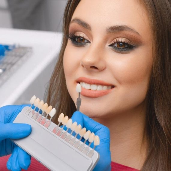 Dentist holding a shade guide up to a smiling woman's teeth
