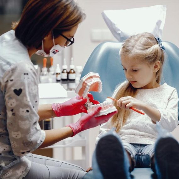 A dentist showing a young girl how to properly brush her teeth.